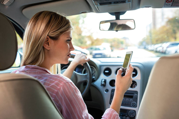 Blonde girl looking at her mobile phone instead of the road, irresponsible driving - 写真・画像