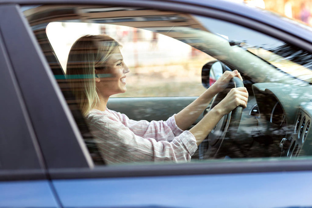 Young blonde girl safely driving her car on the streets of a quiet  - Foto, Imagen
