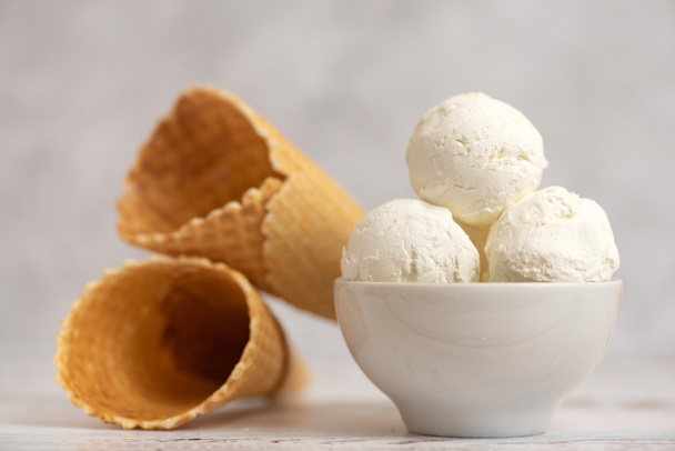 Cuenco de helado de vainilla y conos de waffle sobre fondo claro. Vista lateral
. - Foto, Imagen