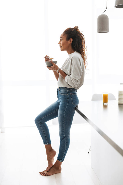 Image of skinny african american woman eating corn flakes with milk on breakfast in stylish kitchen - Fotografie, Obrázek