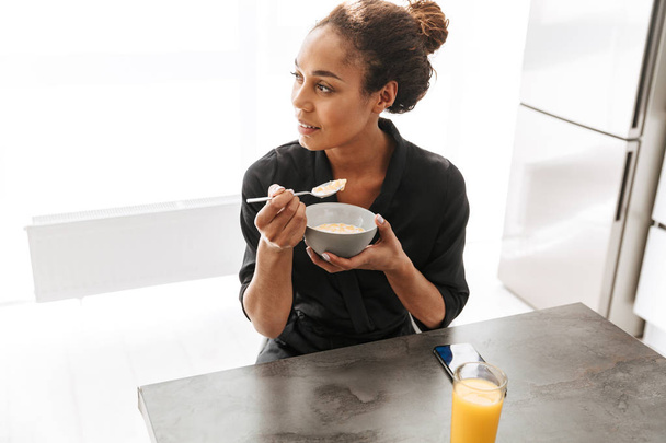 Portrait of pretty african american woman wearing housecoat having breakfast at home - Fotó, kép