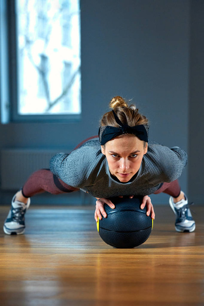 beautiful fit woman in sportswear posing while sitting on the floor with basketball in front of window at gym Healthy girl lifestyle and sport concept - Photo, Image