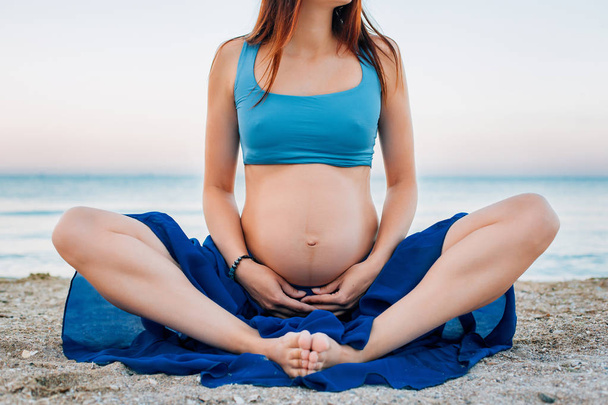 Donna incinta che pratica yoga in spiaggia all'alba. Pancia di una donna incinta vicino al mare
 - Foto, immagini