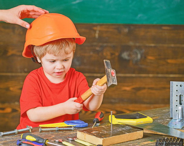 Kid playing with hammer. Daddy holding hardhat on sons head. Concentrated kid in workshop - Foto, afbeelding