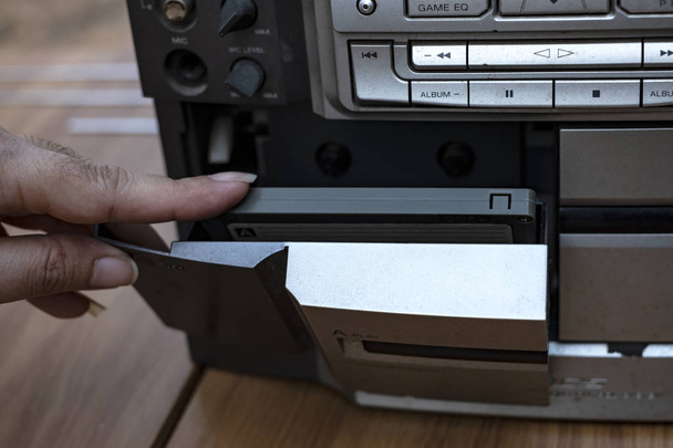 Vrouwen hand cassette ingebruikneming oude ouderwetse tape audiospeler op top bureau houten achtergrond - Foto, afbeelding