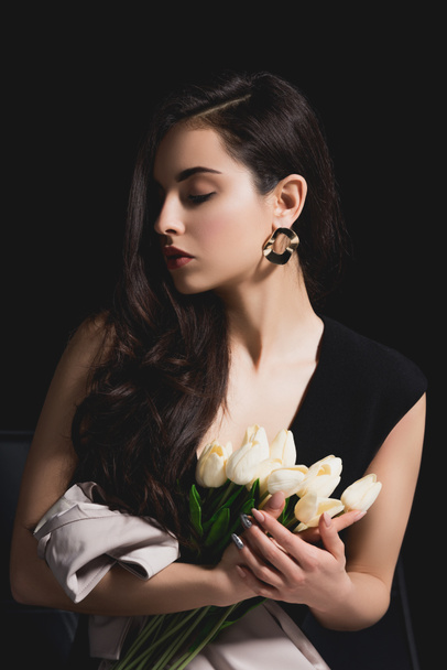 woman in elegant dress sitting and holding bouquet with tulips on black background - Фото, зображення