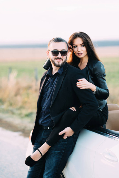Couple sympathique mari et femme passent du temps en dehors de la ville, assis sur un capot de voiture
. - Photo, image