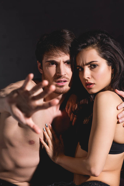shocked woman in black lingerie and shirtless man showing stop sign with hand isolated on black - Photo, Image