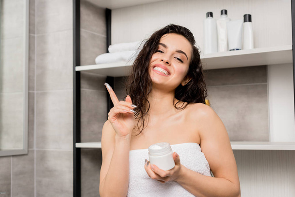 attractive and smiling woman in towel holding cream - 写真・画像
