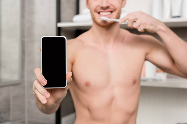 enfoque selectivo del hombre sosteniendo el teléfono inteligente y cepillarse los dientes
  - Foto, Imagen