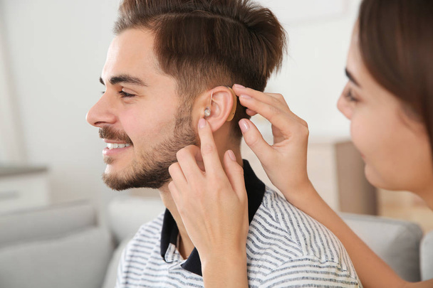 Woman putting hearing aid in man's ear indoors - 写真・画像