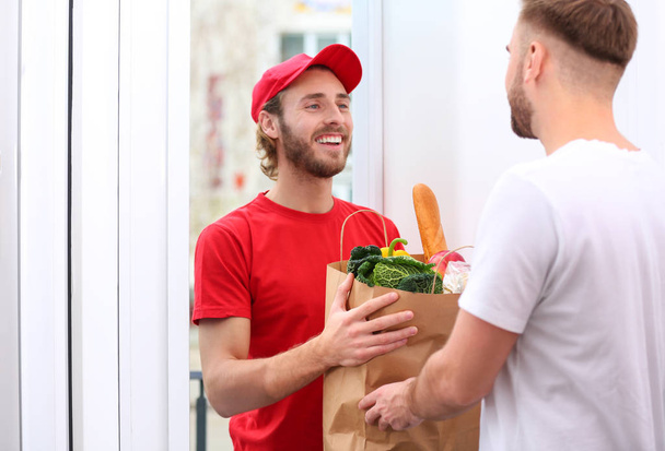 Courier giving paper bag with products to customer at home. Food delivery service - 写真・画像