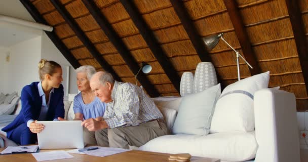 Front view of Caucasian senior couple discussing over clipboard with female doctor at comfortable home. They are relaxing on sofa in living room 4k - Záběry, video