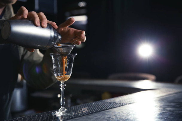 Barman pouring martini espresso cocktail into glass at counter, closeup. Space for text - Фото, зображення