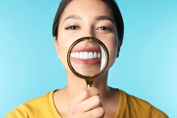 Young woman with healthy teeth and magnifier on color background, closeup - Valokuva, kuva