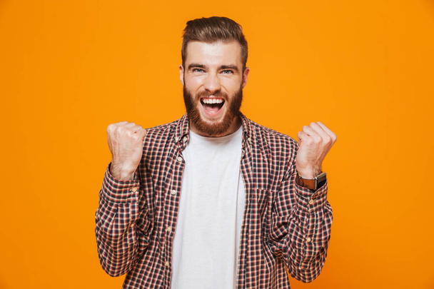 Portrait of a cheerful young man wearing casual clothes standing isolated over yellow background, celebrating success - Foto, imagen