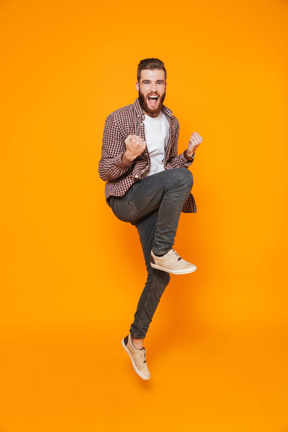 Full length portrait of a cheerful young man wearing casual clothes isolated over yellow background, celebrating success, jump - Foto, imagen