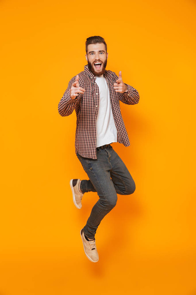 Full length portrait of a cheerful young man wearing casual clothes isolated over yellow background, pointing at camera - Fotoğraf, Görsel