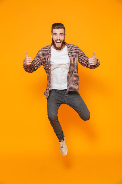 Full length portrait of a cheerful young man wearing casual clothes isolated over yellow background, thumbs up - Foto, Bild