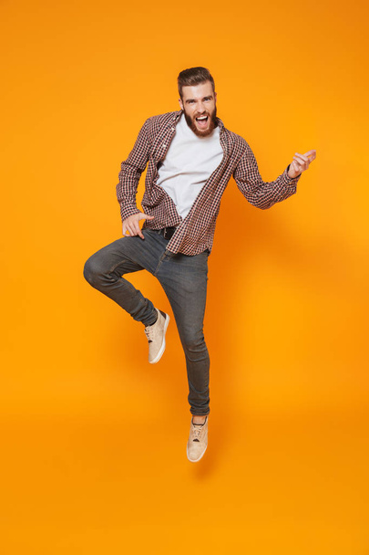 Full length portrait of a cheerful young man wearing casual clothes isolated over yellow background, jump - Zdjęcie, obraz