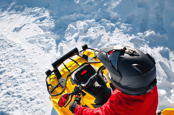 Ein junger Mann in roter warmer Winterkleidung und schwarzem Helm auf dem Geländewagen steht im dichten Schnee mit tiefer Radspur. Moto-Wintersport. Ansicht von oben. - Foto, Bild