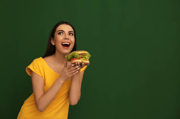 Nuori nainen syö maukasta hampurilaista väritaustalla. Tekstitila
 - Valokuva, kuva