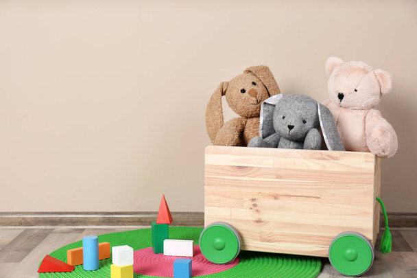 Wooden cart with stuffed toys and constructor on floor against light wall. Space for text - Photo, Image