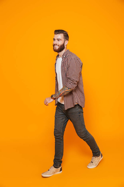 Full length portrait of a cheerful young man wearing casual clothes isolated over yellow background, walking away - Fotografie, Obrázek