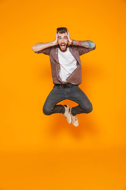 Full length portrait of a cheerful young man wearing casual clothes isolated over yellow background, jumping - Foto, Bild