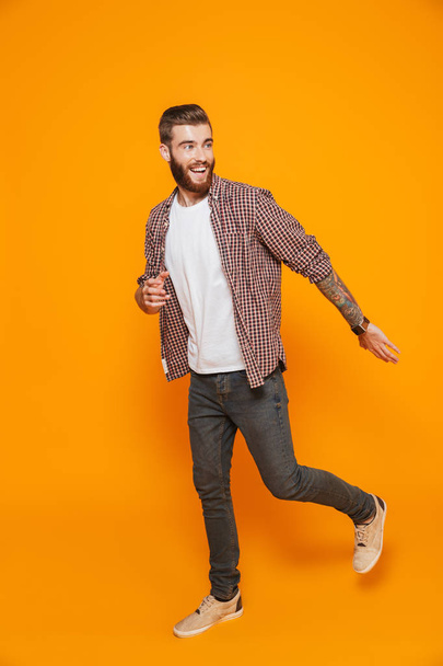 Full length portrait of a cheerful young man wearing casual clothes isolated over yellow background, walking away - Foto, Imagen