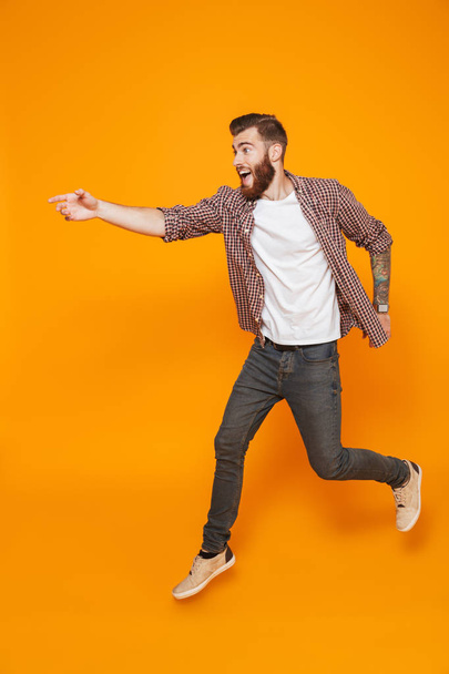 Full length portrait of a cheerful young man wearing casual clothes isolated over yellow background, running away - Zdjęcie, obraz