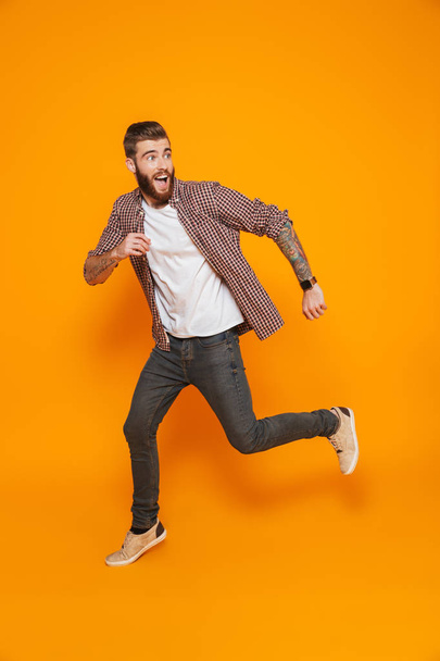 Full length portrait of a cheerful young man wearing casual clothes isolated over yellow background, running away - Fotografie, Obrázek