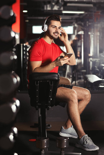 Young man with headphones listening to music on mobile device at gym - Foto, immagini