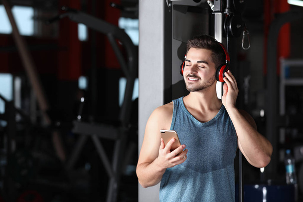 Young man with headphones listening to music on mobile device at gym - Foto, afbeelding