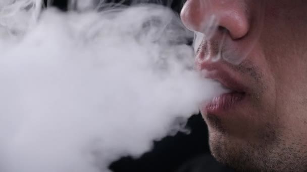 Close-up van man vaper uitademen grote wolken rook met e-sigaret vape op zwarte achtergrond in slow motion - Video