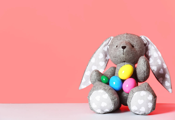 Cute toy Easter bunny and eggs on table against color background, space for text - Фото, зображення