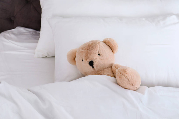 Cute teddy bear lying in bed indoors. Space for text - Фото, изображение