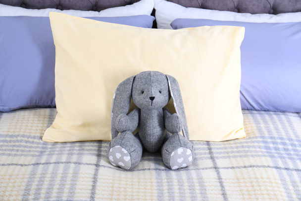 Cute toy rabbit sitting on bed indoors - 写真・画像