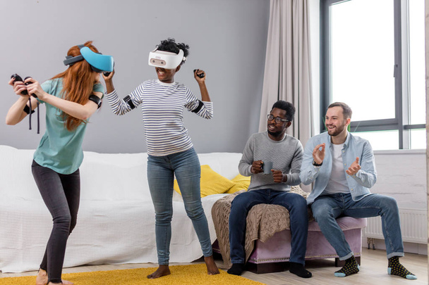 Two multiracial young women dancing wearing virtual reality glasses indoors - Foto, immagini