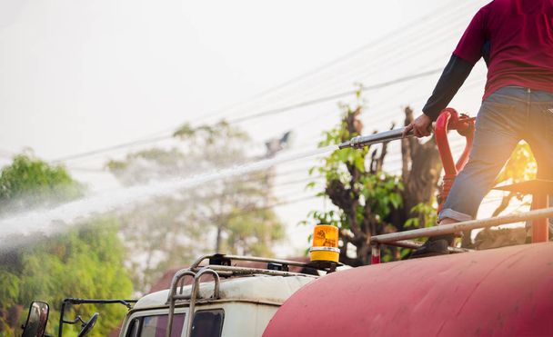 персонал, стоящий на водяном грузовике с проведением пожаротушения сопло и шланг с распылительной водой для очистки дороги
 - Фото, изображение