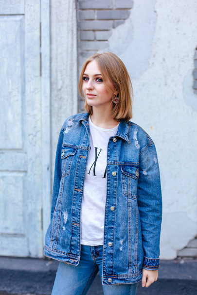 Fashion girl standing near brick wall in denim oversized jacket and beautiful ear rings. - Photo, Image