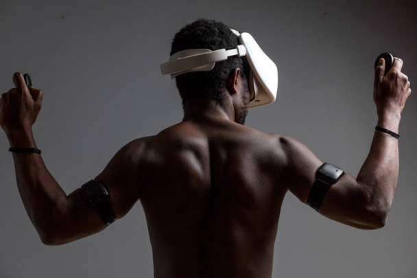 Parte posterior del atleta muscular masculino africano con el torso desnudo usando auriculares vr
 - Foto, Imagen