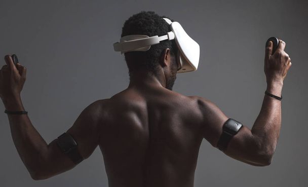 Backside of African male muscular athlet with naked torso using vr headset - Фото, изображение