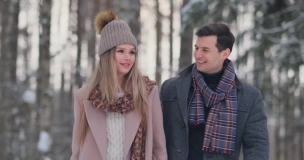 In de winter besneeuwde bos, jonge mannen en vrouwen gekleed in jassen en sjaals zijn wandel- en plezier. Verliefde paar samen doorbrengen dag van Valentijnskaarten. - Video