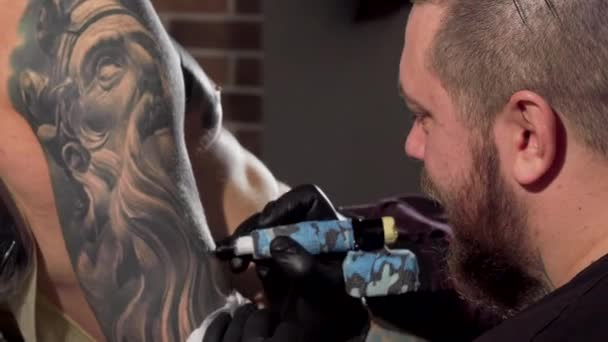 Vista trasera de un tatuador haciendo tatuajes en el brazo del cliente masculino
 - Metraje, vídeo