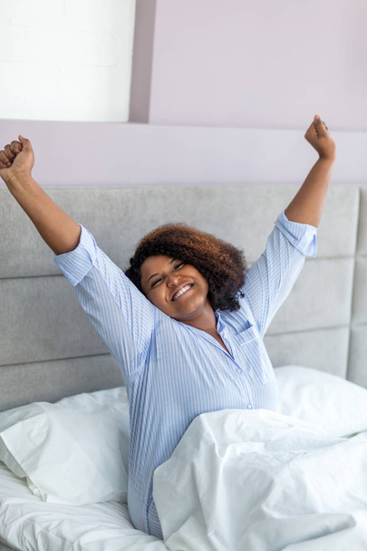 beautiful african woman in stylishpajama stretching while sitting in the bed - Photo, image