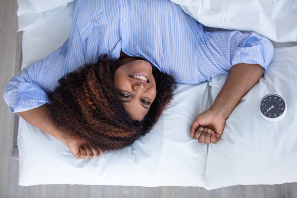 cheerful woman looking at the camera while lying on her bed at home - Photo, Image