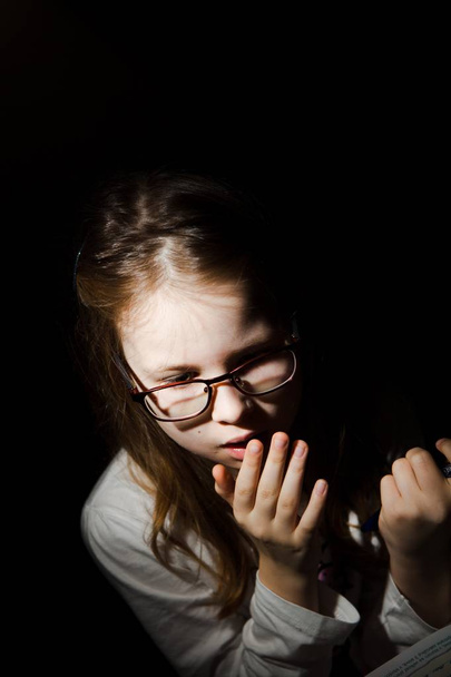 Young girl feared while reading book. Black background. Fear worries and scare. Naturally processed photo. - Photo, Image