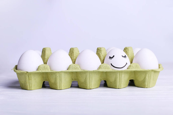 One egg in the tray is different smile, copy space. Happy Easter concept greeting card design. - Fotó, kép