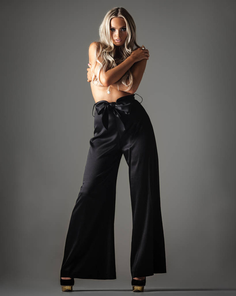 trendy jonge vrouw in broek poseren op grijs - Foto, afbeelding